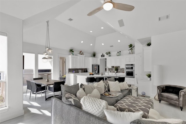 living room with high vaulted ceiling, ceiling fan, and light wood-type flooring