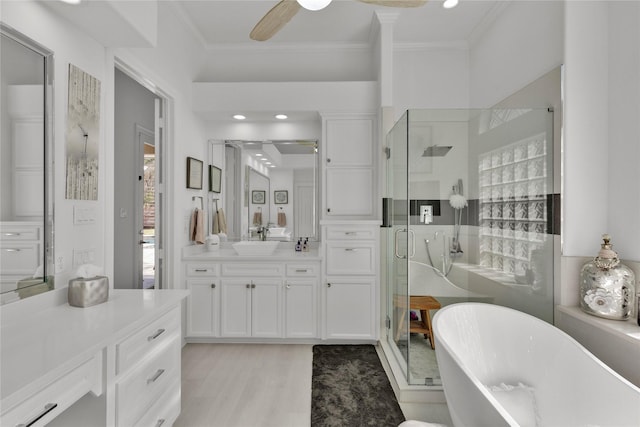 bathroom featuring plus walk in shower, hardwood / wood-style floors, ornamental molding, vanity, and ceiling fan