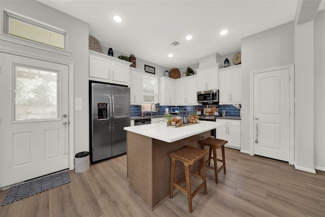 kitchen with white cabinets, a breakfast bar, stainless steel appliances, and a center island