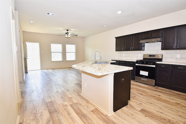 kitchen featuring an island with sink, sink, decorative backsplash, stainless steel gas range, and light hardwood / wood-style flooring