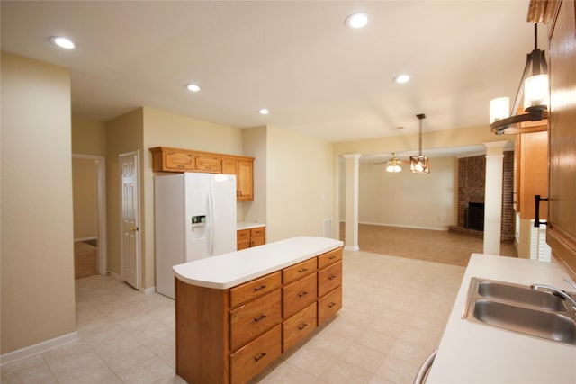 kitchen with sink, a brick fireplace, hanging light fixtures, white fridge with ice dispenser, and decorative columns