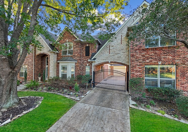 traditional home featuring an attached garage, brick siding, concrete driveway, stone siding, and a gate