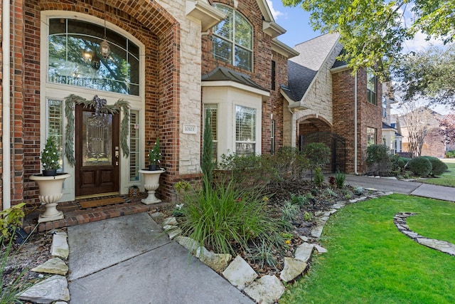 entrance to property featuring brick siding, a lawn, and roof with shingles