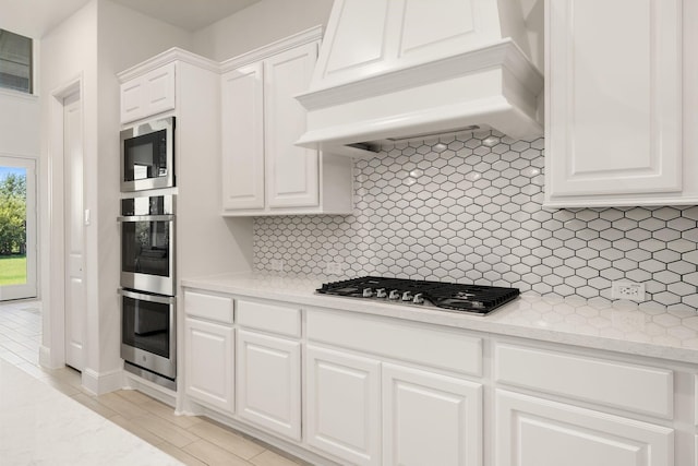 kitchen with white cabinetry, premium range hood, tasteful backsplash, and stainless steel appliances