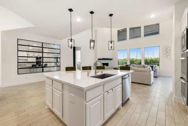 kitchen with sink, light stone counters, stainless steel appliances, a kitchen island with sink, and white cabinets