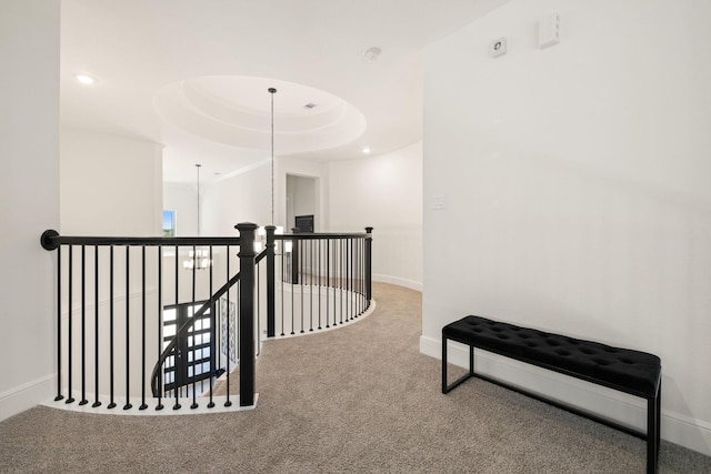 hallway featuring an inviting chandelier, a raised ceiling, and carpet