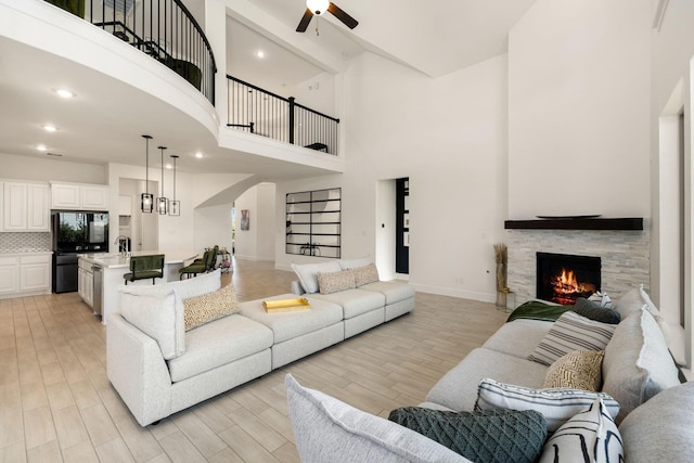 living room featuring a towering ceiling, a fireplace, sink, ceiling fan, and light wood-type flooring