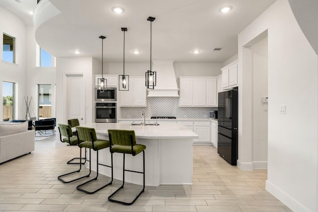 kitchen with black refrigerator, white cabinetry, an island with sink, built in microwave, and oven