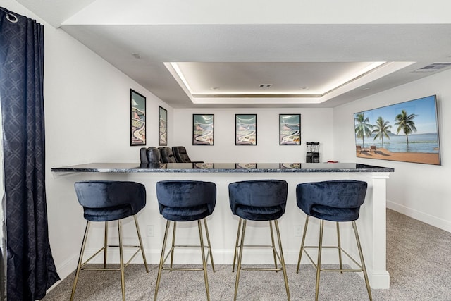 kitchen featuring light colored carpet, a kitchen breakfast bar, a raised ceiling, and kitchen peninsula