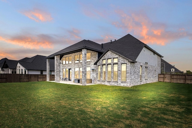 back house at dusk featuring a lawn and a patio