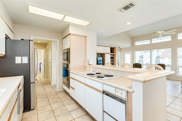 kitchen with white cabinetry, vaulted ceiling, light tile patterned floors, kitchen peninsula, and stainless steel appliances