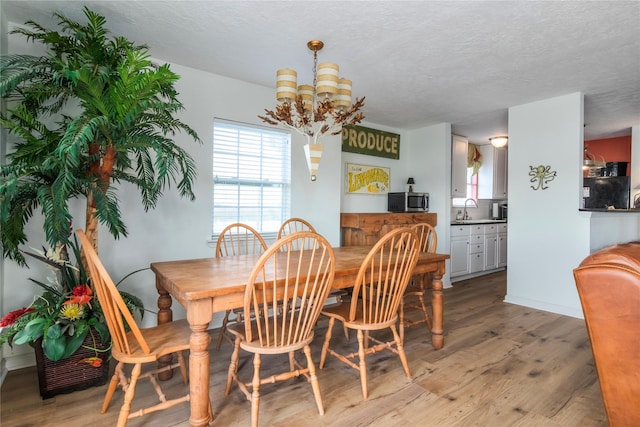 dining room featuring a textured ceiling, light wood finished floors, baseboards, and a notable chandelier