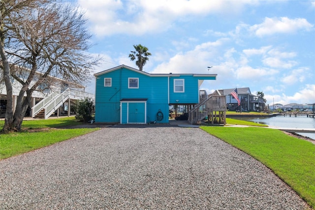 view of front of home with stairs, driveway, a water view, and a front yard