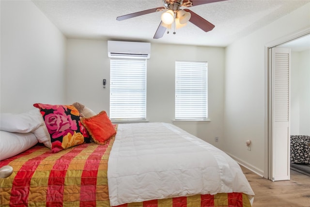 bedroom with a wall unit AC, light wood-style floors, ceiling fan, and a textured ceiling