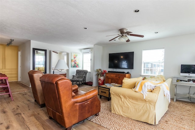 living area featuring an AC wall unit, ceiling fan, light wood-style flooring, and a textured ceiling