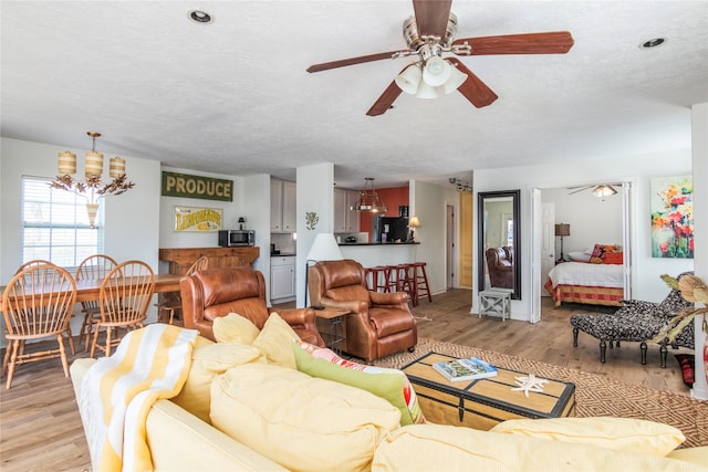 living area featuring light wood-style floors, a textured ceiling, and ceiling fan with notable chandelier