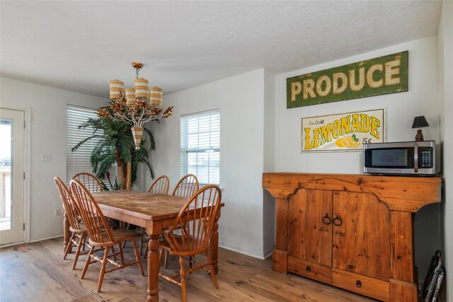 dining space with light wood-type flooring, a textured ceiling, baseboards, and a notable chandelier