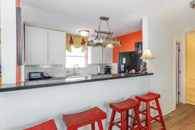 kitchen with light wood-style floors, white cabinetry, a sink, and backsplash