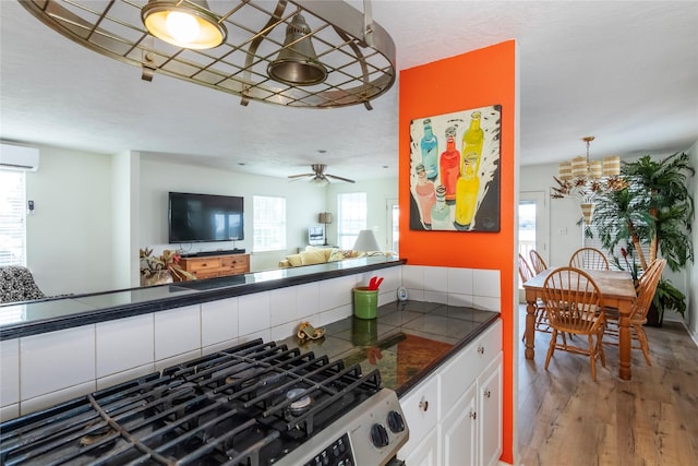 kitchen featuring ceiling fan, a wall unit AC, wood finished floors, white cabinets, and open floor plan