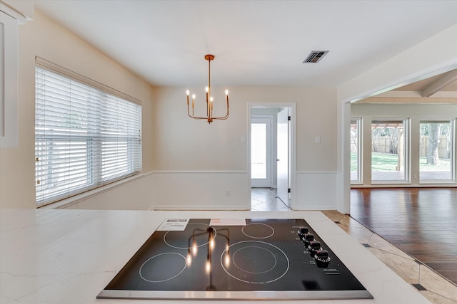 kitchen with pendant lighting, a healthy amount of sunlight, black electric stovetop, and an inviting chandelier