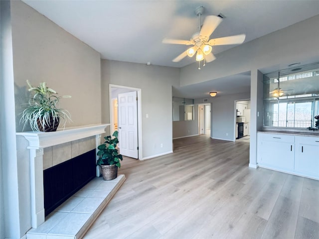 living room featuring a ceiling fan, light wood-type flooring, a fireplace, and baseboards