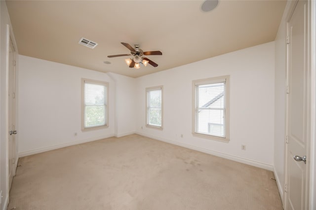 empty room with baseboards, visible vents, a ceiling fan, and light colored carpet