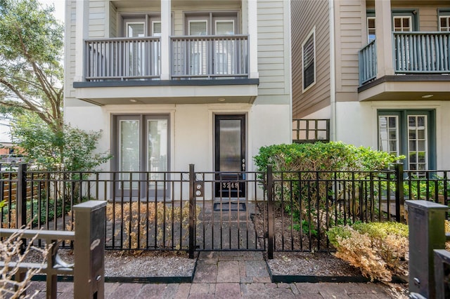 doorway to property featuring a gate, fence, a balcony, and stucco siding