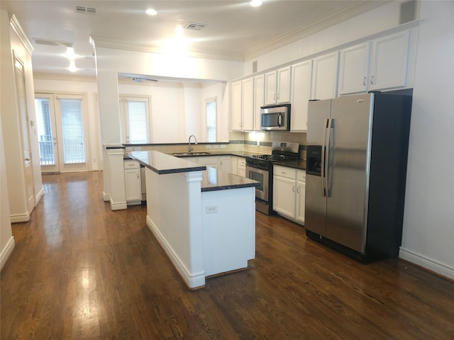 kitchen with white cabinets, appliances with stainless steel finishes, a center island, a peninsula, and crown molding