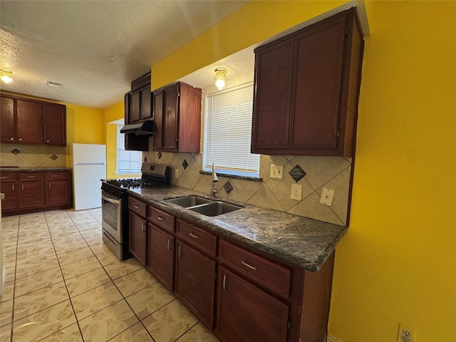 kitchen featuring stainless steel range with gas cooktop, sink, decorative backsplash, white fridge, and light tile patterned floors