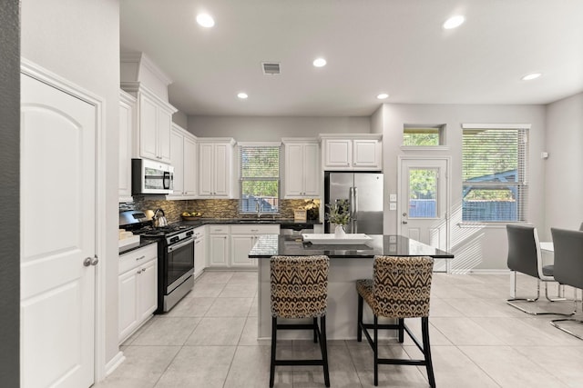 kitchen with stainless steel appliances, visible vents, white cabinetry, tasteful backsplash, and a kitchen bar