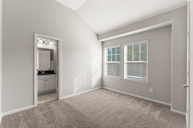 unfurnished bedroom with light colored carpet, vaulted ceiling, a sink, ensuite bath, and baseboards