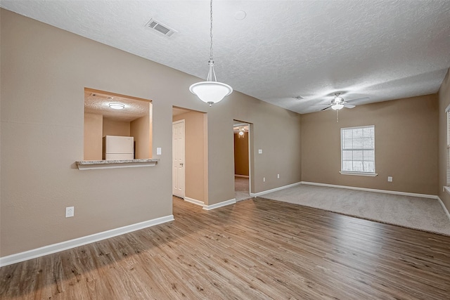 unfurnished room with wood finished floors, a ceiling fan, visible vents, and baseboards