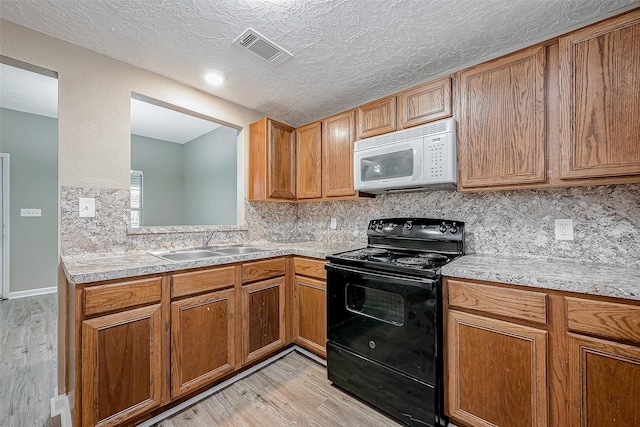 kitchen featuring white microwave, visible vents, black range with electric stovetop, light countertops, and a sink