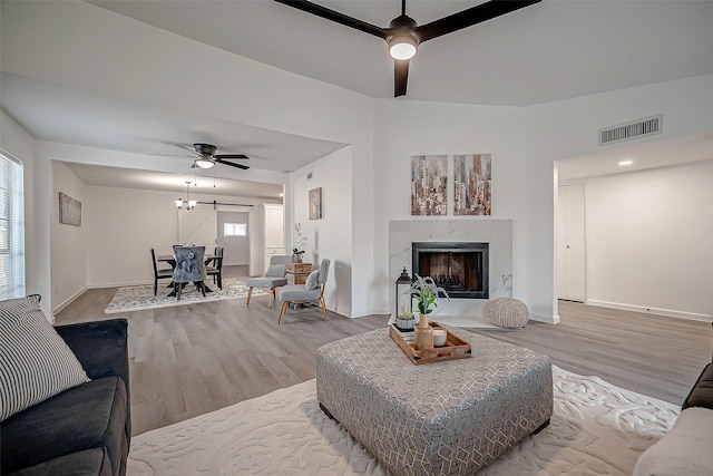 living room with a premium fireplace, ceiling fan, and light wood-type flooring