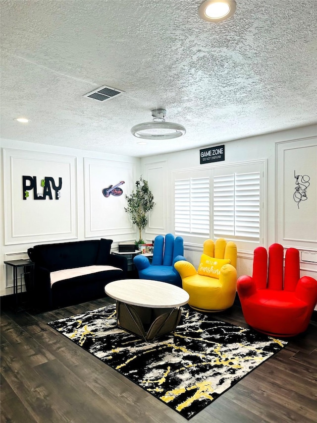 living area featuring dark wood-type flooring, visible vents, a decorative wall, and a textured ceiling