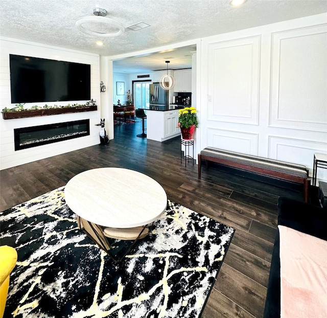 living area with dark wood finished floors, a textured ceiling, and a glass covered fireplace