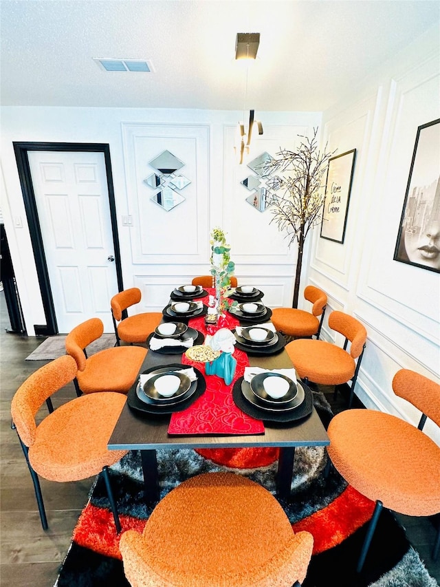 dining space with dark wood-type flooring, visible vents, and a decorative wall