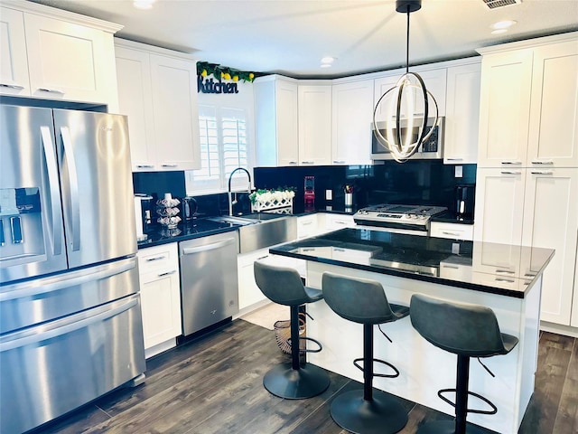 kitchen featuring white cabinets, hanging light fixtures, appliances with stainless steel finishes, a center island, and dark wood finished floors