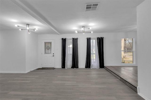 empty room with a notable chandelier, beam ceiling, and light wood-type flooring