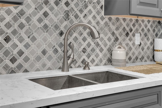 room details featuring gray cabinets, tasteful backsplash, light stone countertops, and sink