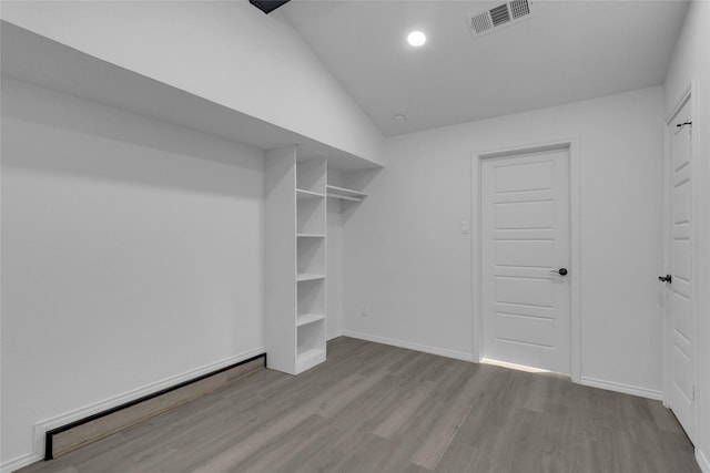 spacious closet with lofted ceiling, a baseboard heating unit, and light hardwood / wood-style flooring