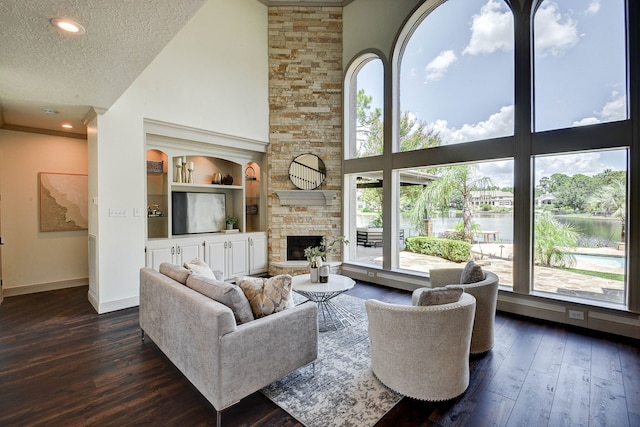 living room with dark hardwood / wood-style flooring, a stone fireplace, a textured ceiling, and a high ceiling