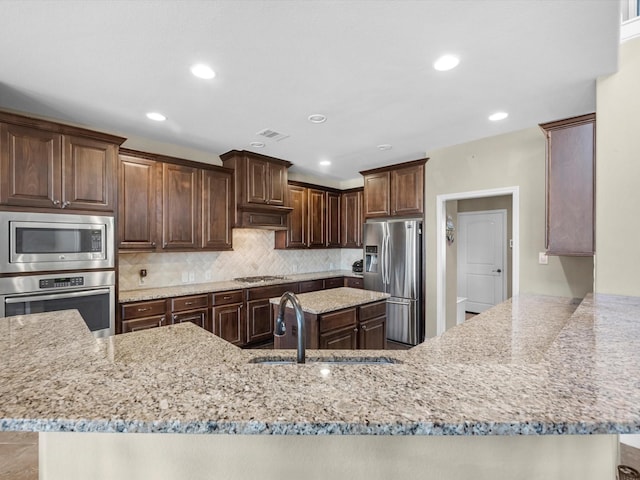 kitchen featuring sink, tasteful backsplash, appliances with stainless steel finishes, kitchen peninsula, and light stone countertops