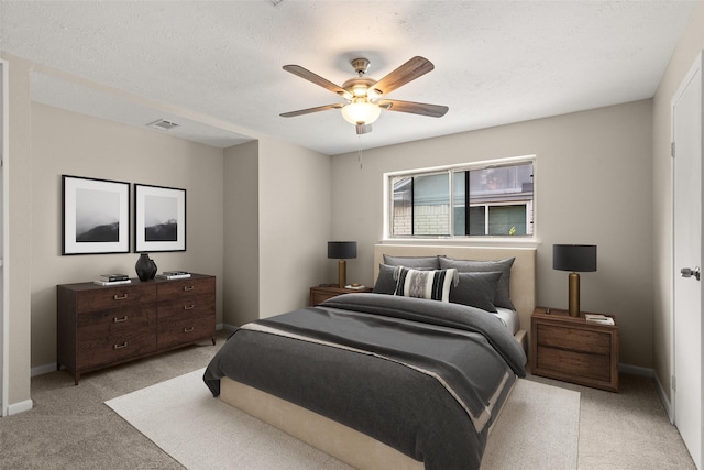 bedroom with ceiling fan, light carpet, and a textured ceiling