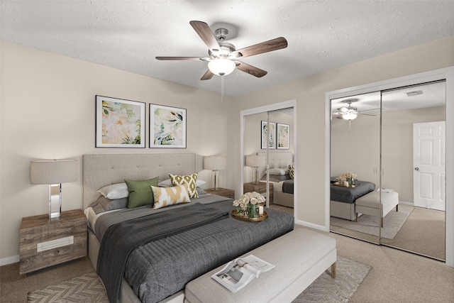 bedroom with ceiling fan, two closets, light colored carpet, and a textured ceiling