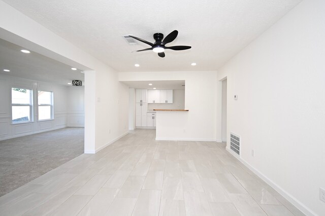 unfurnished living room with ceiling fan, light colored carpet, and a textured ceiling