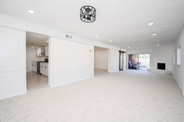 unfurnished living room with light colored carpet, a barn door, and a textured ceiling