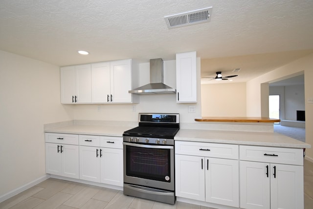 kitchen with stainless steel gas range oven, wall chimney range hood, white cabinets, and a textured ceiling