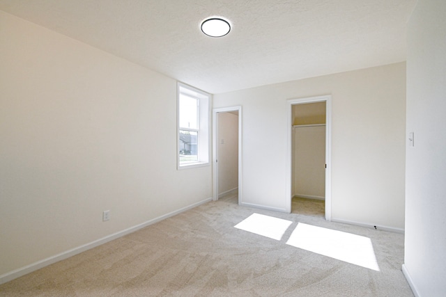 unfurnished bedroom with a closet, a spacious closet, light carpet, and a textured ceiling