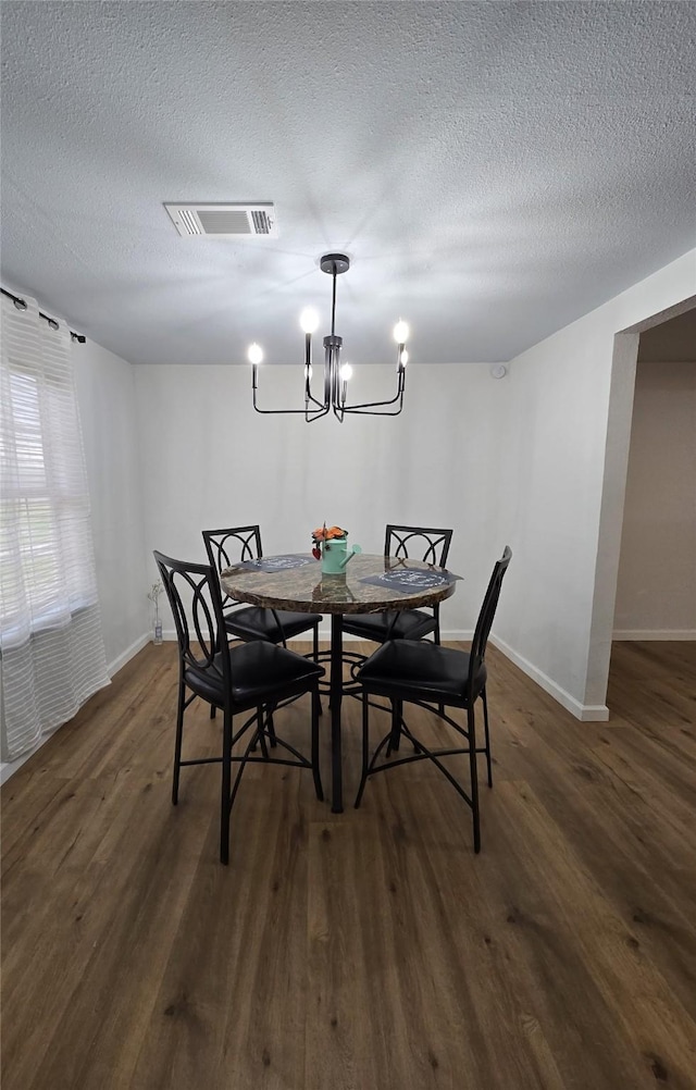 dining area featuring a textured ceiling, dark wood-type flooring, visible vents, baseboards, and an inviting chandelier